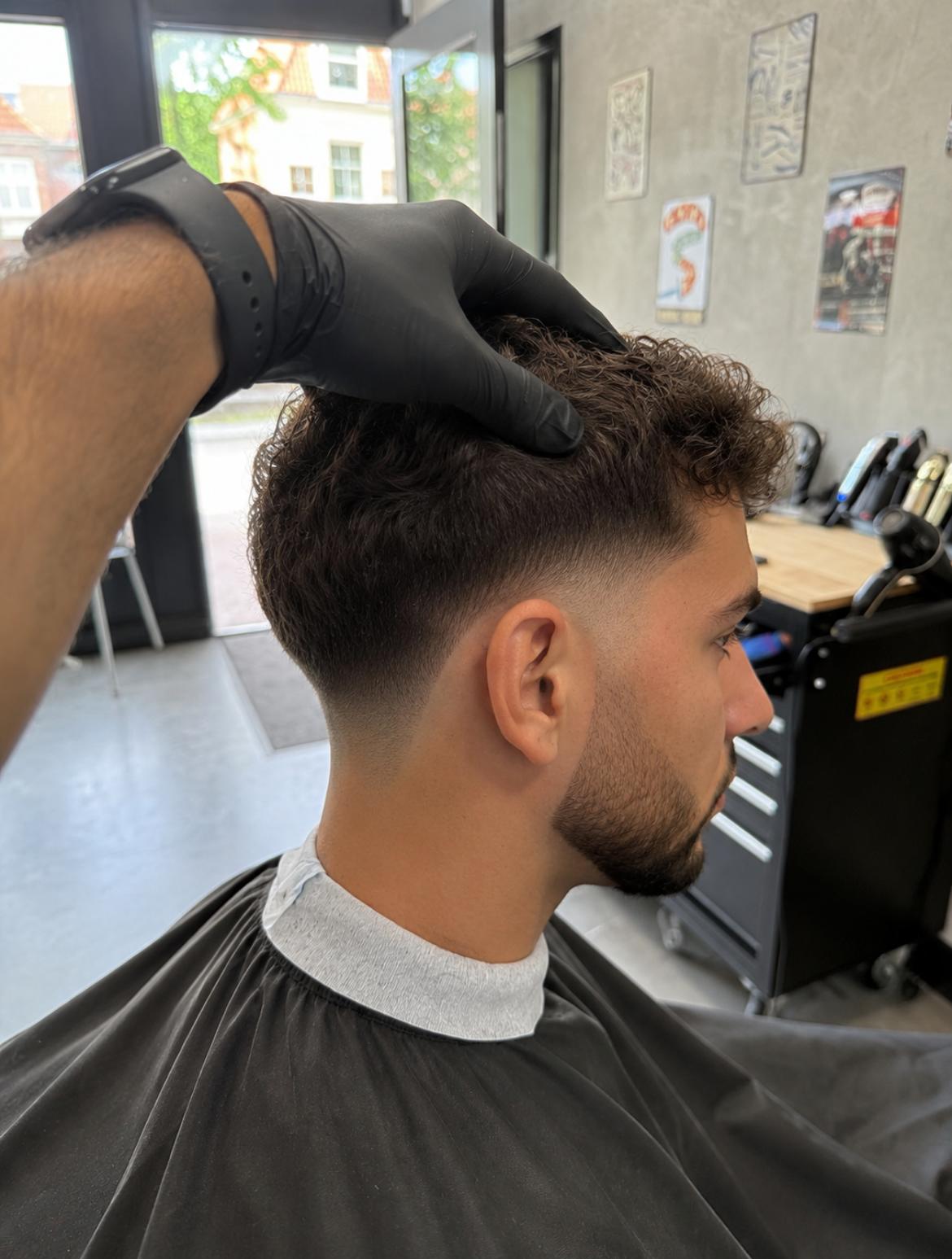 Krullend herenkapsel met een vloeiende low fade en korte baard bij Berkay's Barbershop in Hoorn