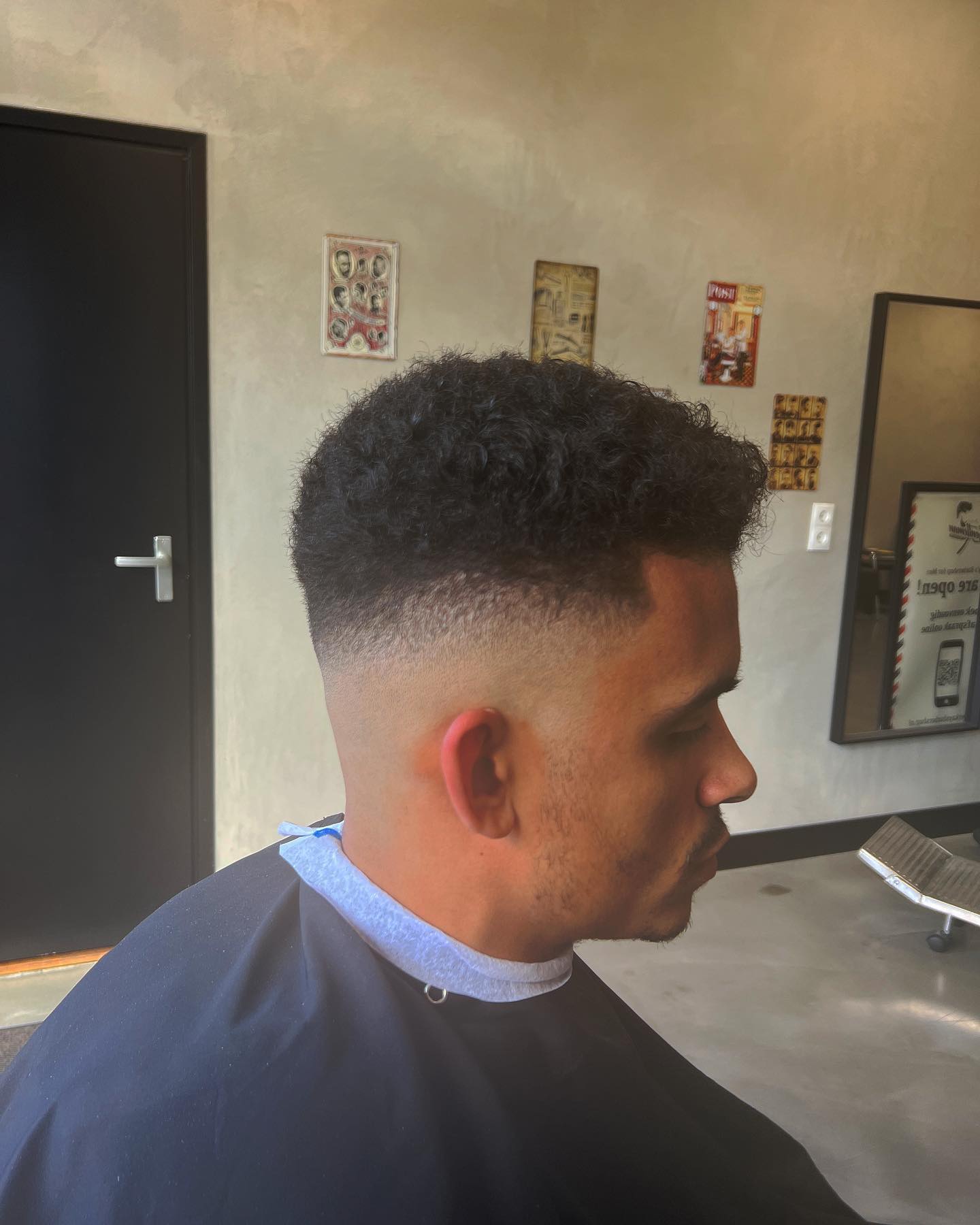 Donker krullend haar bovenop met een frisse high fade aan de zijkanten