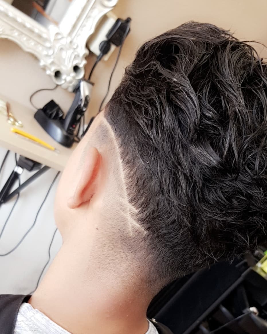 Detail van een taper fade rond het oor met donker golvend haar bovenop